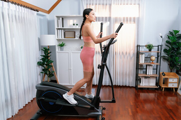 Energetic and strong athletic asian woman running on elliptical running machine at home. Pursuit of fit physique and commitment to healthy lifestyle with home workout and training. Vigorous - obrazy, fototapety, plakaty