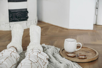 Cozy winter still life. Kids legs in warm woolen socks and checkered white pyjamas. Mug of hot...