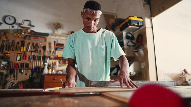 Concentrated Young Brazilian Carpenter Learning Profession in Workshop, using saw machine slicing wood