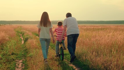 Dad teaches child ride bike on path. Little boy learns to ride kids bike. Mother, father, son...