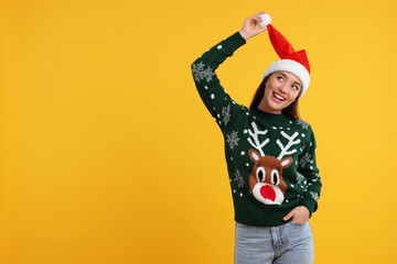 Happy young woman in Christmas sweater and Santa hat on orange background. Space for text