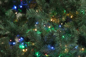 Christmas tree with bright string lights, closeup. Bokeh effect