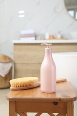 Fototapeta na wymiar Bottle of shower gel and brush on wooden table near tub in bathroom
