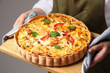 Woman holding board with tasty quiche on grey background, closeup