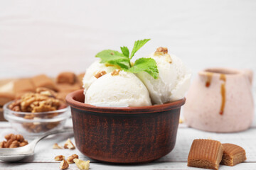 Bowl of tasty ice cream with caramel sauce, mint and nuts on white wooden table, closeup