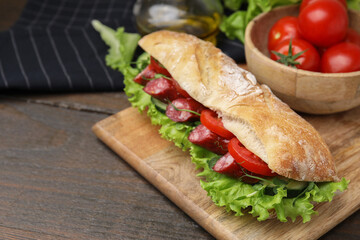 Delicious sandwich with sausages and vegetables on wooden table, closeup. Space for text