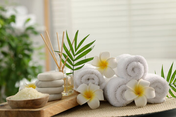 Composition with different spa products, plumeria flowers and palm leaves on table indoors