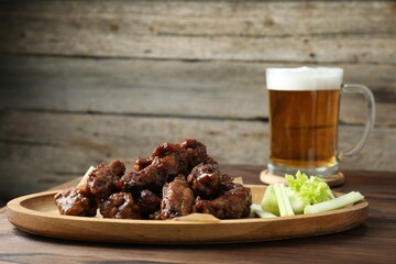 Delicious chicken wings served with cut celery stalks and beer on wooden table