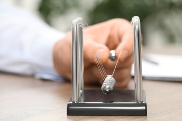 Man playing with Newton's cradle at table, closeup. Physics law of energy conservation