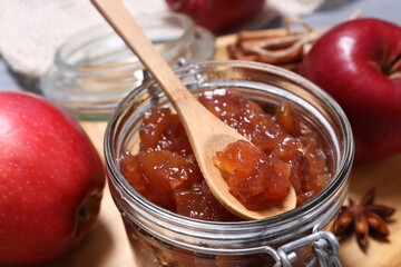 Delicious apple jam and spoon in jar on table, closeup