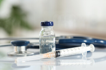 Glass vial, syringe and stethoscope on white table, closeup