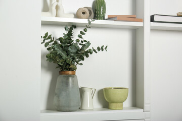 White shelves with books, eucalyptus and different decor indoors. Interior design