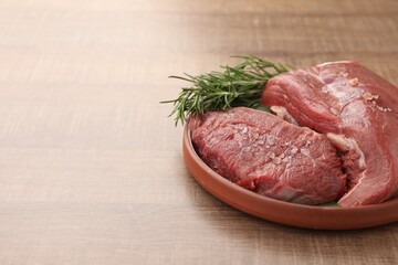 Pieces of raw beef meat with spices and rosemary on wooden table, space for text