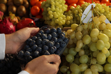 Woman picking fresh grapes at market, closeup