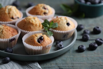 Delicious sweet muffins with blueberries and mint on light blue wooden table, closeup