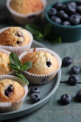 Delicious sweet muffins with blueberries and mint on light blue wooden table, closeup