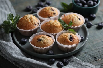 Delicious sweet muffins with blueberries and mint on light blue wooden table