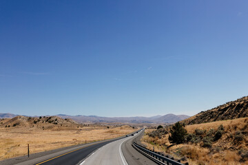 A picturesque asphalt road among the mountains. Highway in autumn on a sunny day with cars and trucks