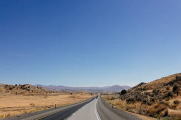 A picturesque asphalt road among the mountains. Highway in autumn on a sunny day with cars and trucks