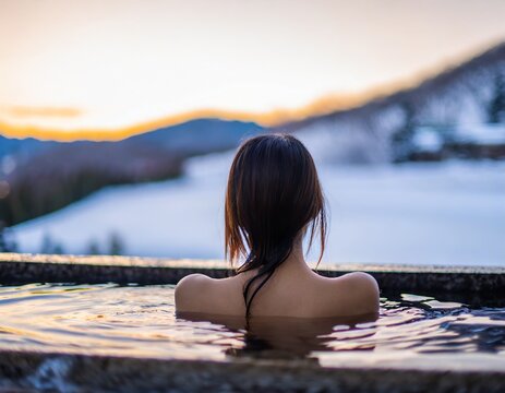  雪景色のきれいな温泉に浸かっている日本人女性の後ろ姿
