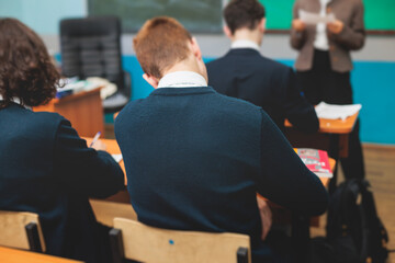 Kids in school writing and taking notes, teens pupils behind desks during the lesson listen to...