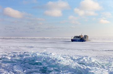 Tourists travel by Khivus airboat across frozen Baikal Lake from village of Listvyanka to village of Goloustnoye on cold sunny January day. Scenic winter landscape. Natural background. Winter travel