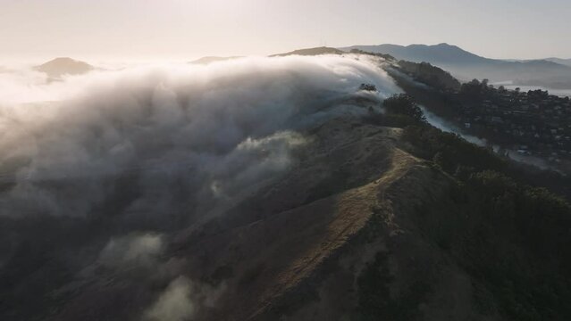 Aerial view of fog clouds rolling down the mountain hills of Sausalito, San Franco suburban, California, West coast, USA. Overhead view of mist covered mountains and San Franco Bay suburb at morning