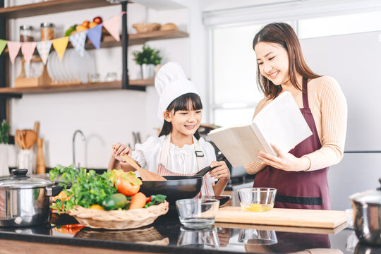 Mother and daughter cooking in kitchen preparation food for dinner meal, lifestyles together child with parent