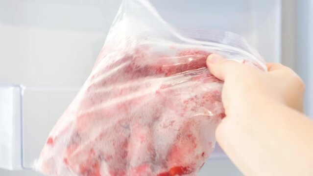 Female hand takes out a plastic bag with a zip fastener with frozen strawberries from the refrigerator, close-up.