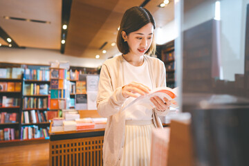 Portrait of young adult southeast asian woman reading book at bookstore shop