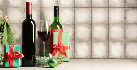Bottle and glass of wine with Christmas gifts on grey tile background with space for text