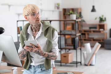 Young tattooed man working with tablet computer in office
