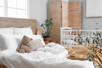 Interior of light bedroom with bed and baby crib