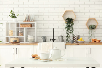 Interior of light kitchen with teapot, cup and snacks on table - obrazy, fototapety, plakaty