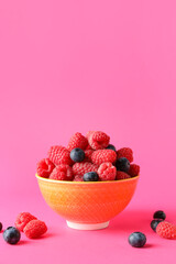 Bowl with fresh raspberries and blueberries on pink background