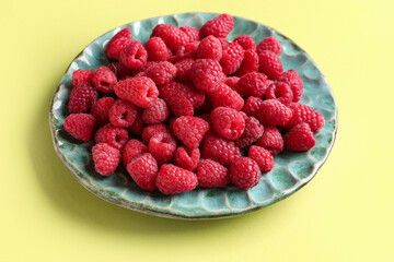 Plate with fresh raspberries on yellow background