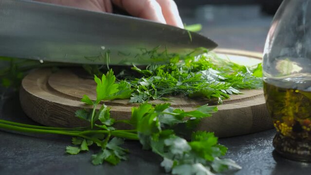Chef chopping parsley with knife on cutting board