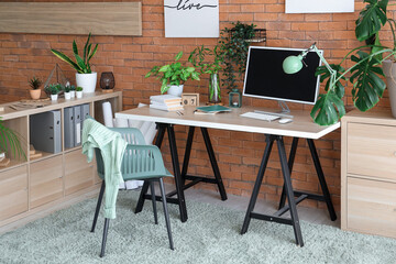 Interior of stylish office with modern workplace, shelving unit and houseplants