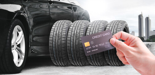 Hand holding a credit card with a row of tires and a black car on the background , Concept of car maintenance and credit card payments - obrazy, fototapety, plakaty