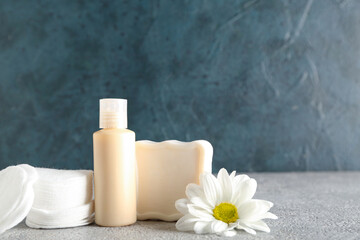 Bottle of cosmetic product, soap, cotton pads and chamomile flower on table
