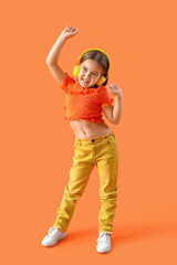 Cute little girl in headphones dancing on orange background