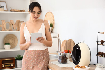 Beautiful young woman using tablet computer near coffee machine in kitchen - Powered by Adobe
