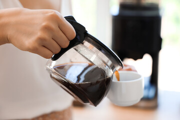 Woman pouring espresso from pot into cup in kitchen