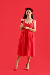Young woman with glass of wine on red background