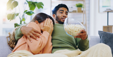 Fear, jump and couple watching tv on a sofa with popcorn for movie, film or streaming show at home....