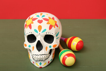 Painted human skull for Mexico's Day of the Dead (El Dia de Muertos) with maracas on wooden table...