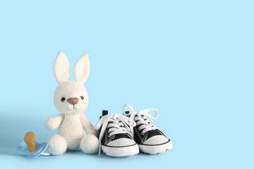 Stylish baby shoes with pacifier and cute toy on blue background