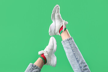 Legs of young woman in stylish white sneakers on green background