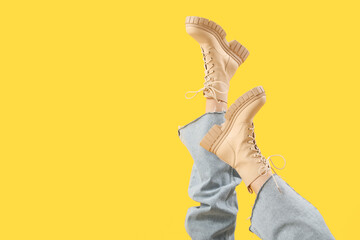 Legs of young woman in stylish beige leather boots on yellow background