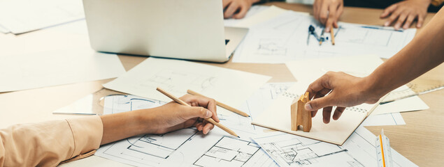 Professional architect hand draws a blueprint on table with architectural document and wooden block...